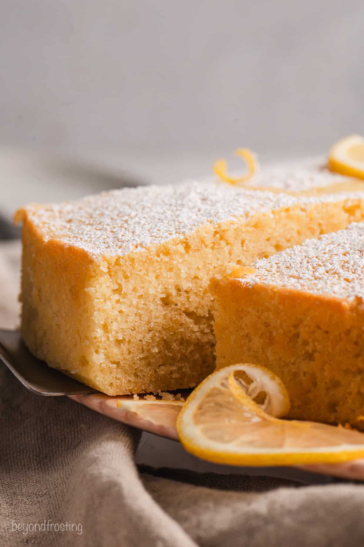 Side view of a slice of lemon olive oil cake partially removed from the rest of the cake with a cake server.