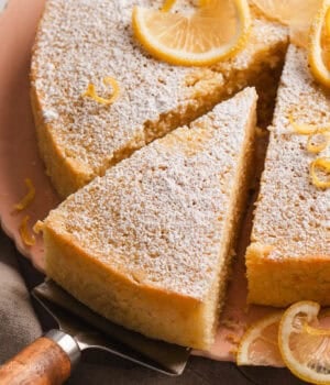 A slice of lemon olive oil cake partially removed from the rest of the cake with a cake server.