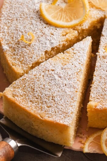 A slice of lemon olive oil cake partially removed from the rest of the cake with a cake server.