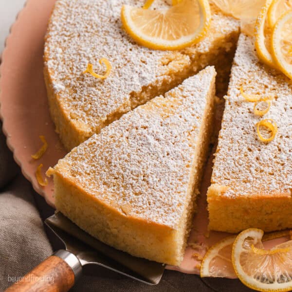 A slice of lemon olive oil cake partially removed from the rest of the cake with a cake server.