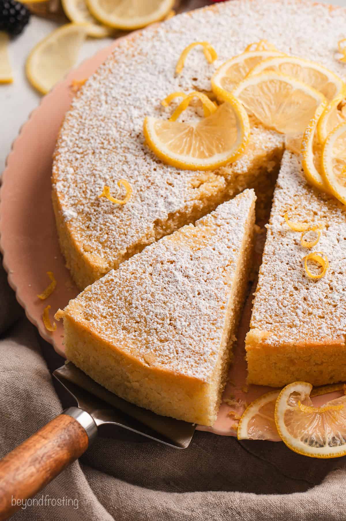 A slice of lemon olive oil cake partially removed from the rest of the cake with a cake server.