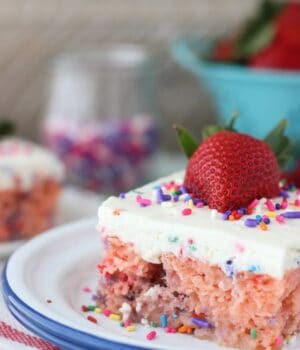 A slice of Funfetti Strawberry Poke Cake: a strawberry cake with sprinkles and topped with a whipping cream topping, sprinkles, and a large strawberry.