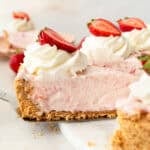 Side view of a slice of strawberry marshmallow pie being lifted from the rest of the pie with a cake server.