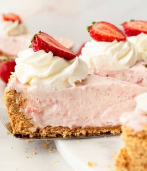 Side view of a slice of strawberry marshmallow pie being lifted from the rest of the pie with a cake server.