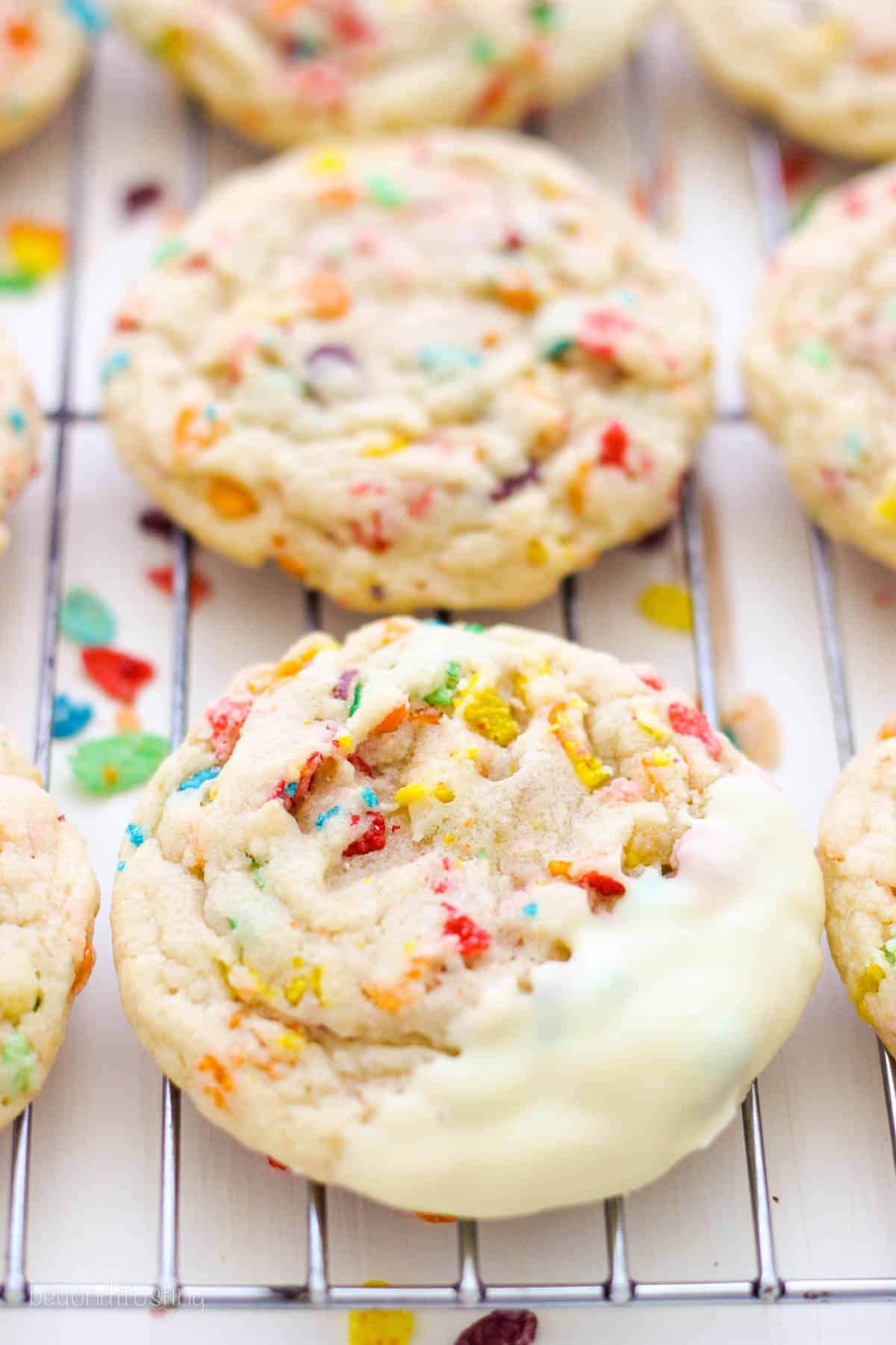 White chocolate-dipped Fruity Pebble sugar cookies in rows on a wire rack.