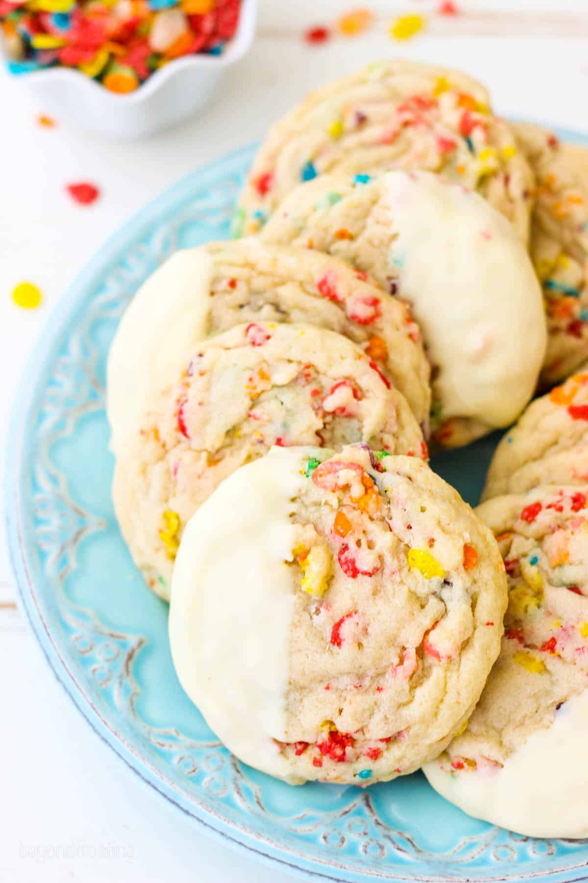 Overhead view of white chocolate-dipped Fruity Pebble sugar cookies arranged on a blue plate.