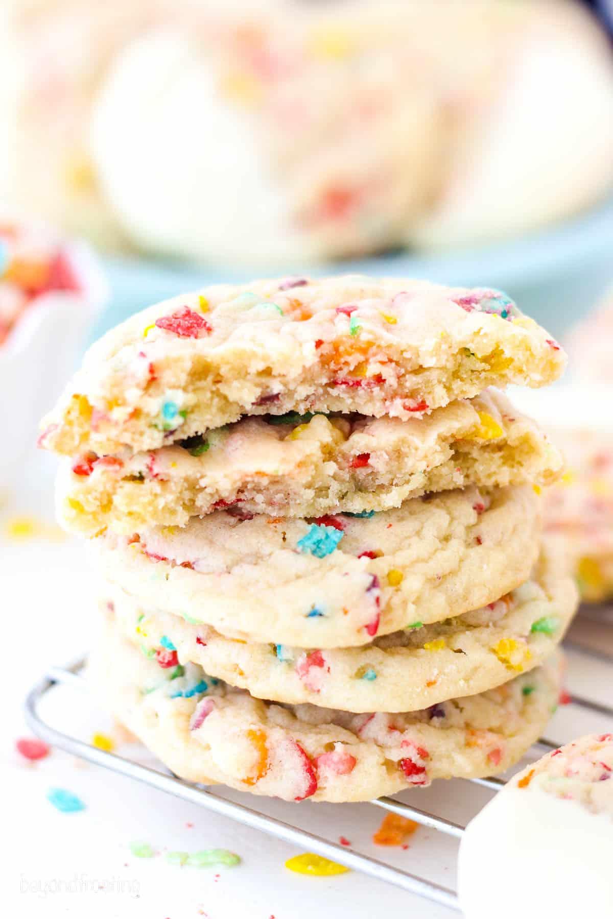 A stack of Fruity Pebble cookies on a wire rack, with the top cookie broken in half.