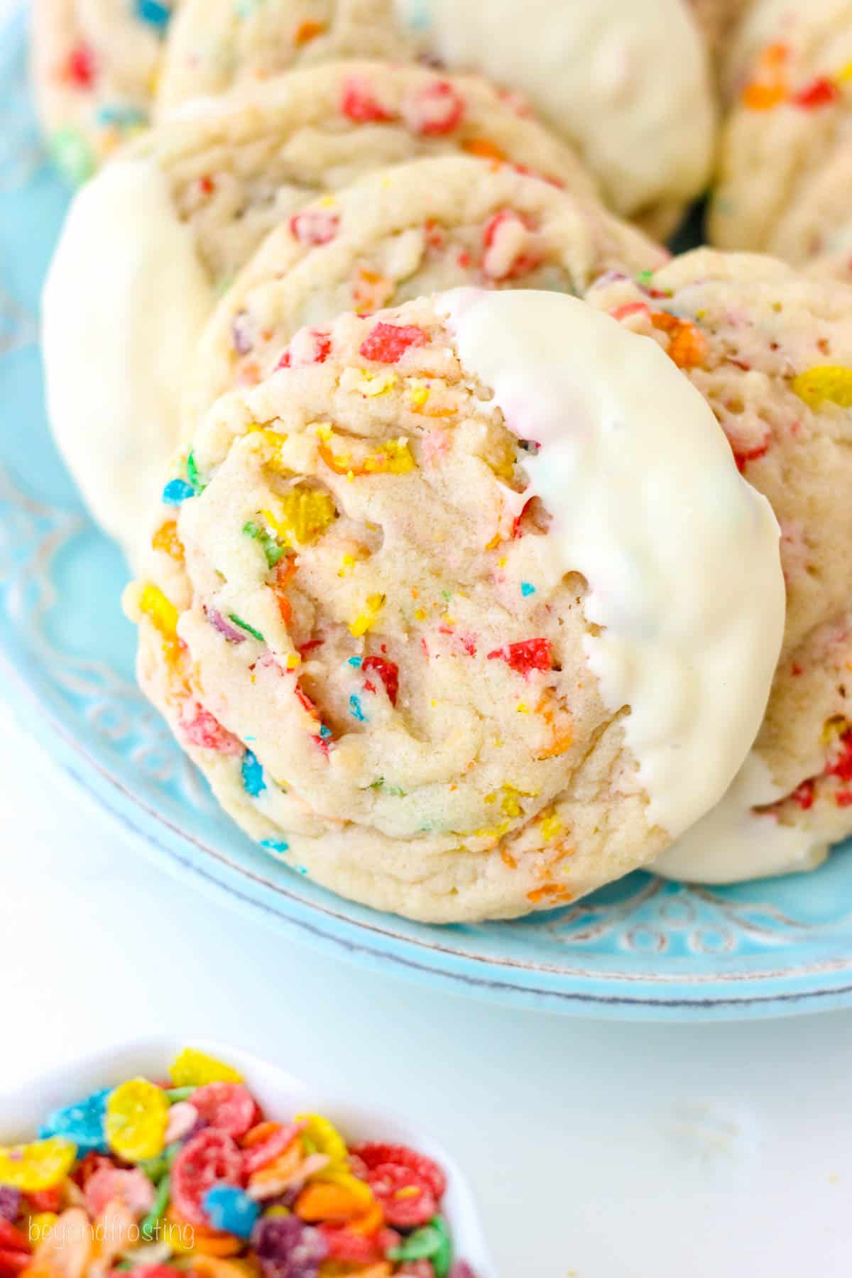 Close up overhead view of white chocolate-dipped Fruity Pebble cookies arranged on a blue plate.