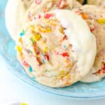 Close up overhead view of white chocolate-dipped Fruity Pebble cookies arranged on a blue plate.