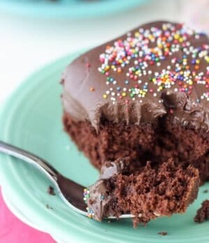 A slice of Chocolate Cake with Chocolate Cream Cheese Frosting with a forkful taken out and topped with sprinkles.