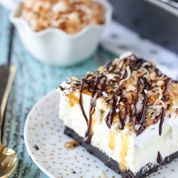 This No-Bake Samoa lush is an icebox cake featuring an Oreo cookie crust, a layer of caramel cheesecake, coconut mousse and a whipped cream topped with caramel, hot fudge and toasted coconut