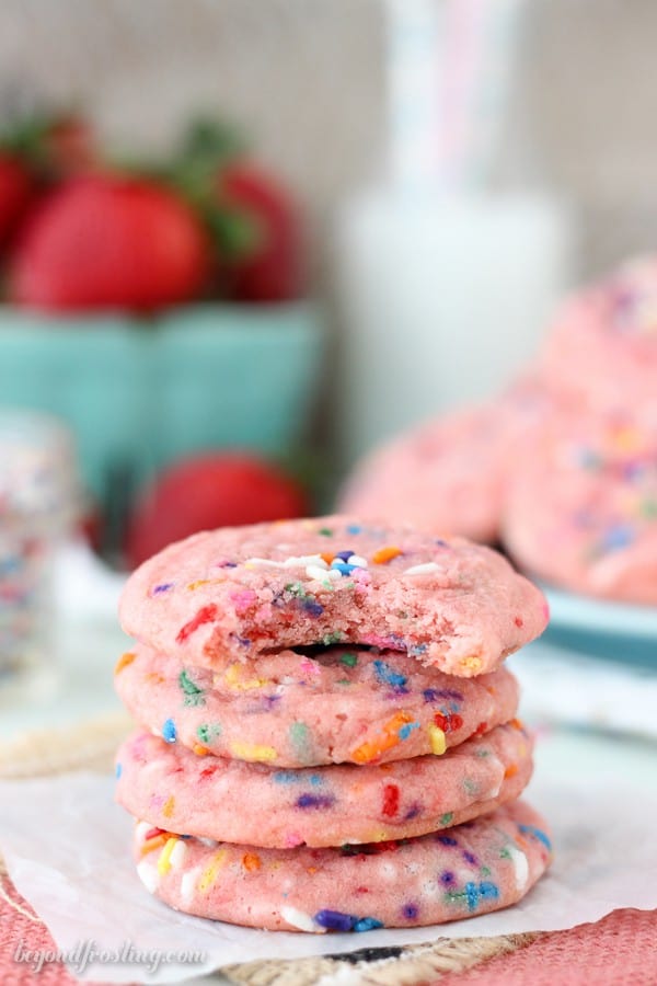 A stack of four pink cookies with sprinkles, one with a bite taken out.