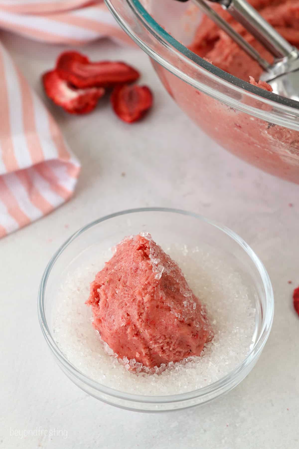 A ball of strawberry cookie dough in a bowl of sanding sugar.