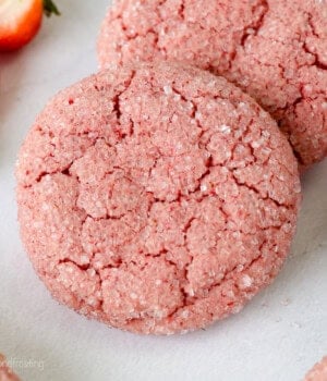Two strawberry cake mix cookies next to a fresh strawberry.
