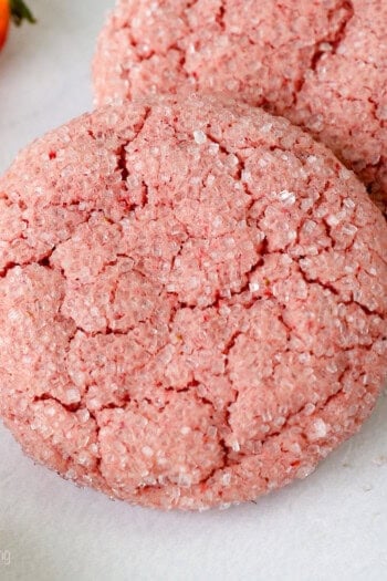 Two strawberry cake mix cookies next to a fresh strawberry.