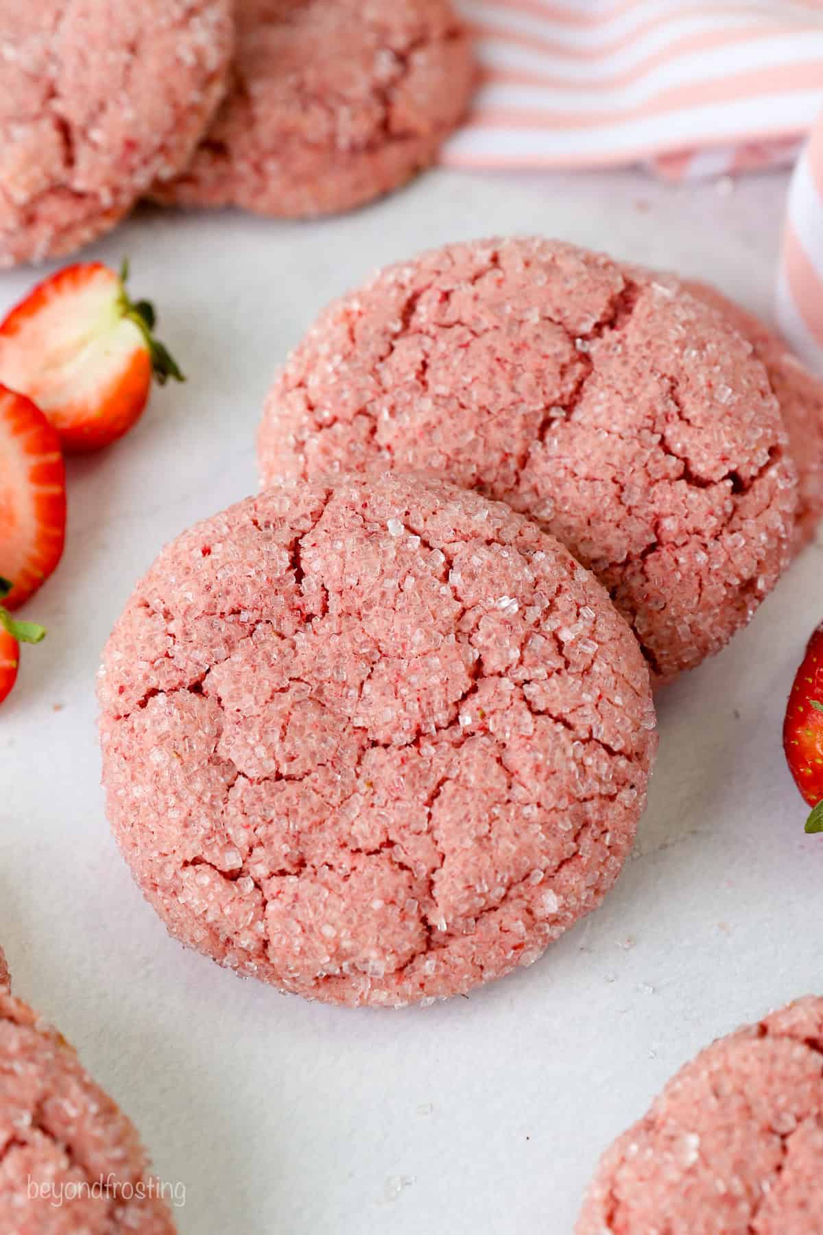 Two strawberry cake mix cookies next to a fresh strawberry, surrounded by more cookies.