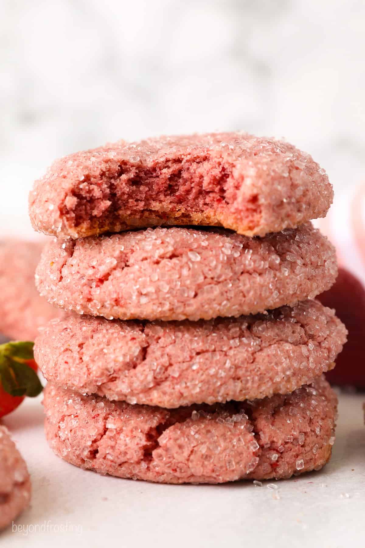 A stack of four strawberry cake mix cookies with a bite missing from the top cookie.