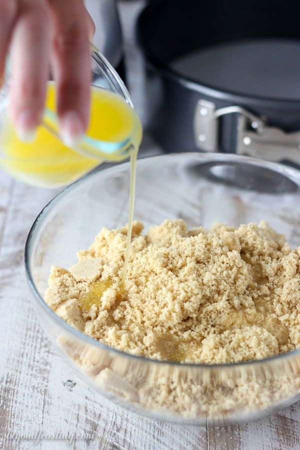 Melted butter being poured into a glass bowl filled with Golden Oreo cookie crumbs