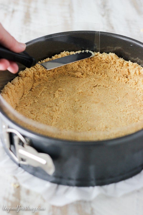 An angled spatula pressing the sides of an Oreo crust in a springform pan