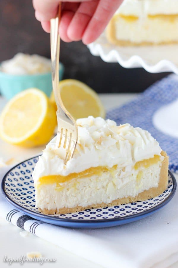 A fork sinking into a slice of cheesecake layered with a lemon curd and shredded coconut.