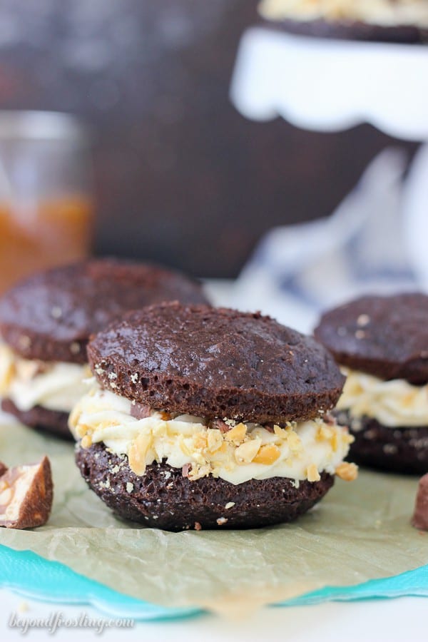 Snicker Whoopie Pies are a delicate chocolate cake with caramel buttercream, salty peanuts and snickers bars.