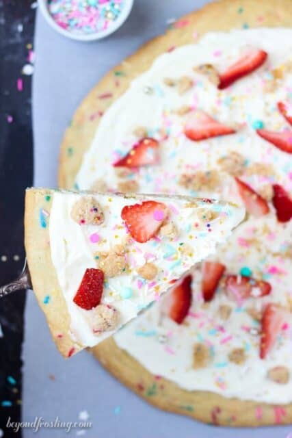 Dessert pizza is so easy! A thick sugar cookie pizza crust loaded with sprinkles. This Funfetti pizza is topped with a marshmallow buttercream, sprinkles and fruit.