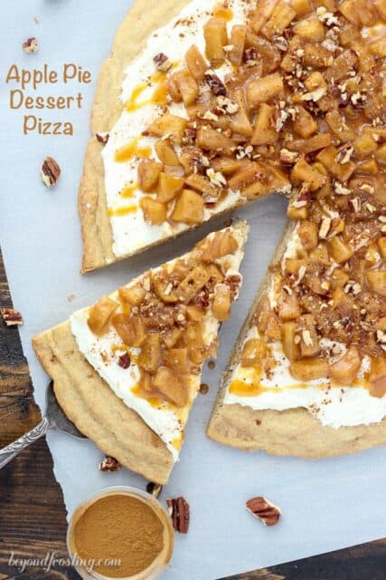 An apple pie dessert pizza on a table with a bowl of caramel sauce beside it