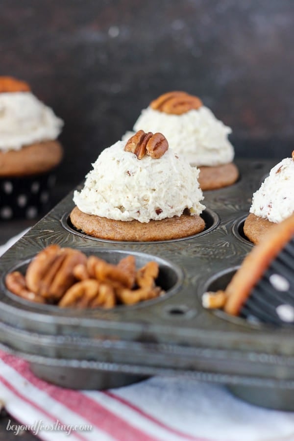 A six-count muffin tin containing some frosted pecan cupcakes as well as some whole pecans