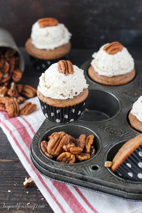 Three maple pecan cupcakes on top of a red and white cloth napkin and a metal muffin tin