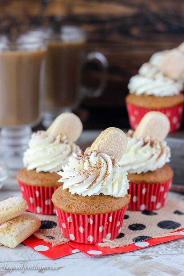 Three pumpkin cupcakes lined up in red polka dot wrappers, a whipped topping dusted with cocoa powder and lady fingers 