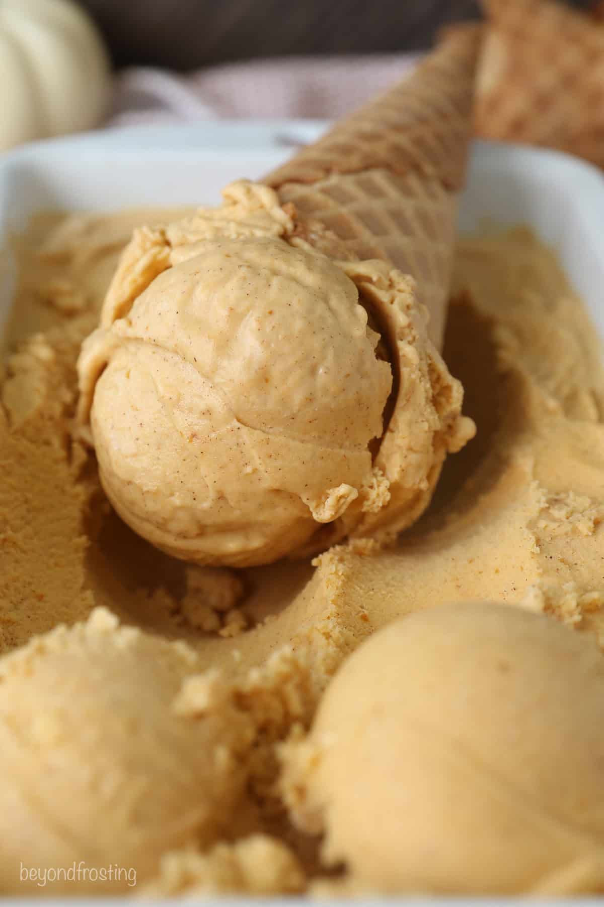 A pumpkin ice cream cone resting in a loaf pan filled with pumpkin pie ice cream.