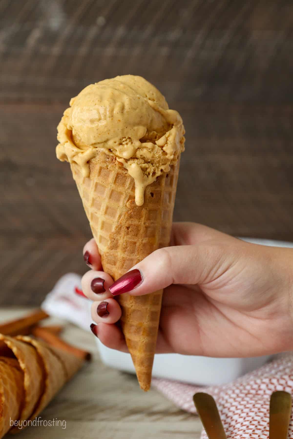 A hand holding up a scoop of pumpkin ice cream in an ice cream cone.