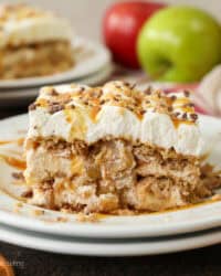 A slice of apple pie lasagna on a plate, with fresh red and green apples next to a second slices in the background.