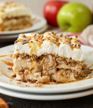 A slice of apple pie lasagna on a plate, with fresh red and green apples next to a second slices in the background.