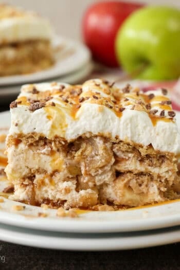 A slice of apple pie lasagna on a plate, with fresh red and green apples next to a second slices in the background.