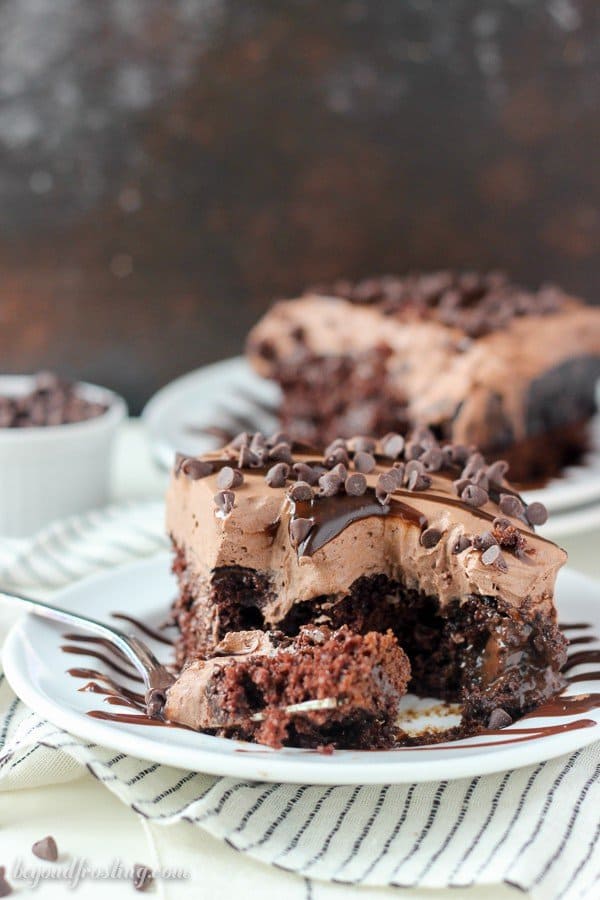 A slice of chocolate poke cake with a fork laying next to it with a bite on it