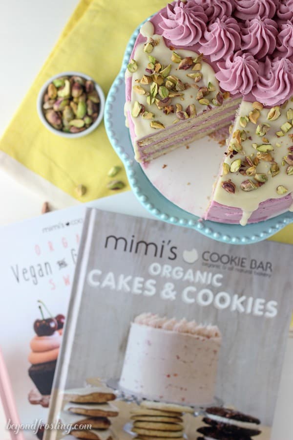 This Blueberry Pistachio Layer cake is a white cake layered with a fresh blueberry frosting and covered with white chocolate ganache and pistachios. Recipe from Mimi's Cookie Bar