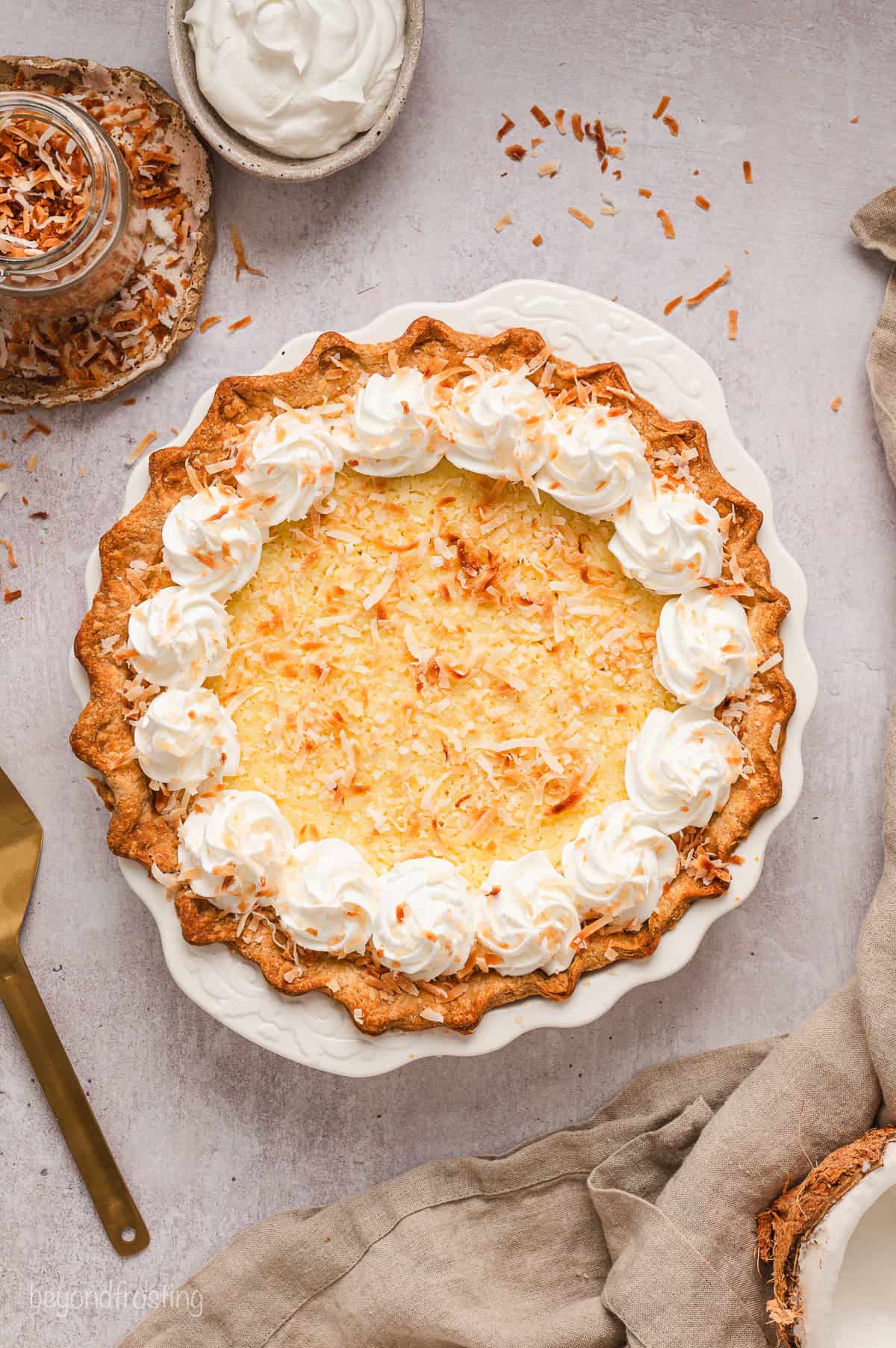 Overhead view of coconut custard pie in a pie plate decorated with a border of piped whipped cream swirls.