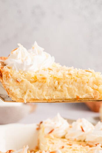 Side view of a slice of coconut custard pie being lifted from the rest of the pie below.