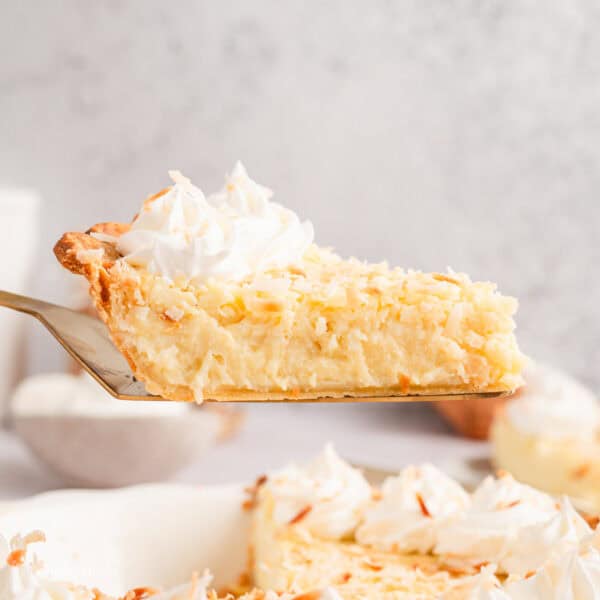 Side view of a slice of coconut custard pie being lifted from the rest of the pie below.