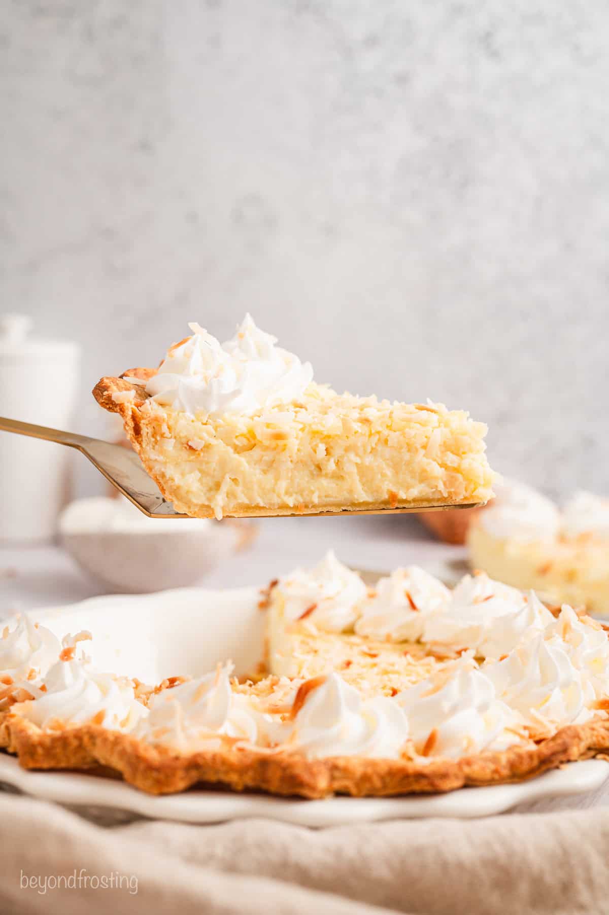 Side view of a slice of coconut custard pie being lifted from the rest of the pie below.