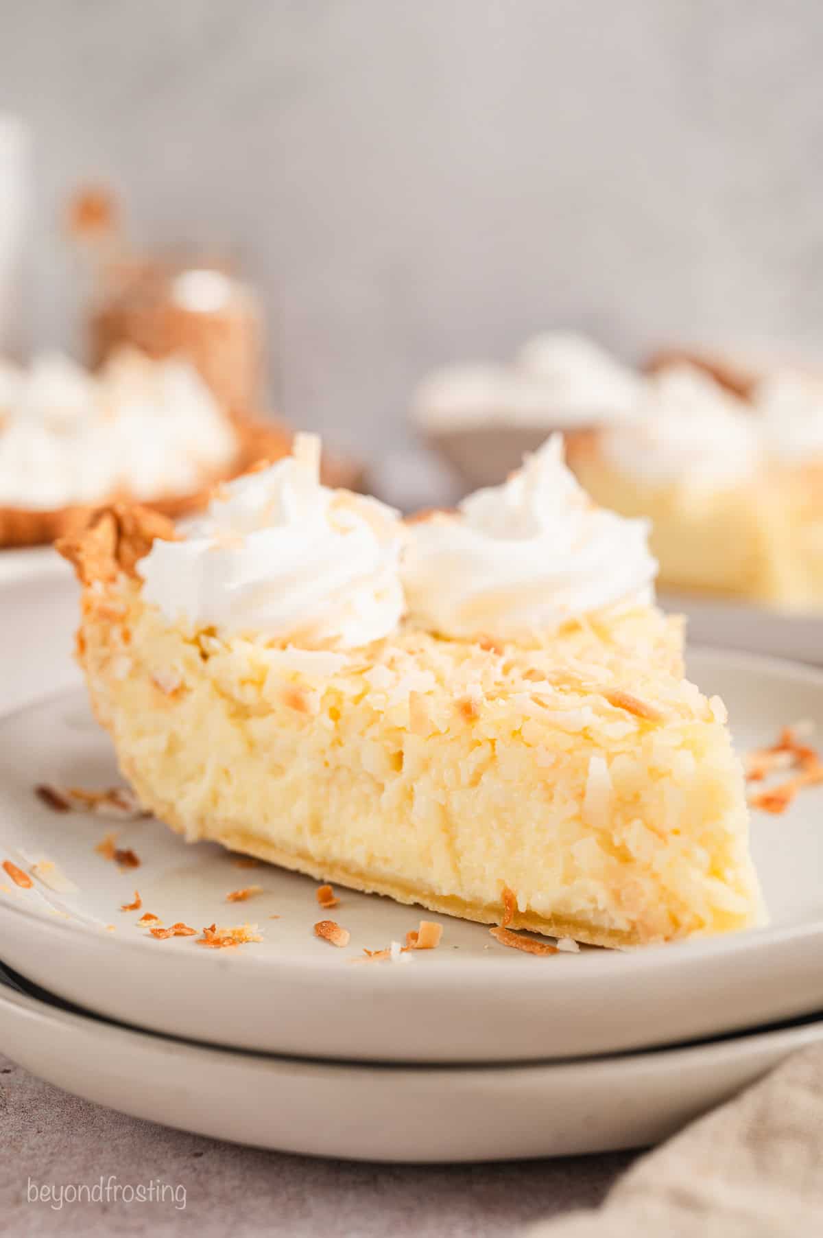 A slice of coconut custard pie topped with swirls of whipped cream on a white plate.