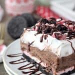 slice of dessert lasagna topped with hot fudge, Oreos, and peppermint candy on a plate