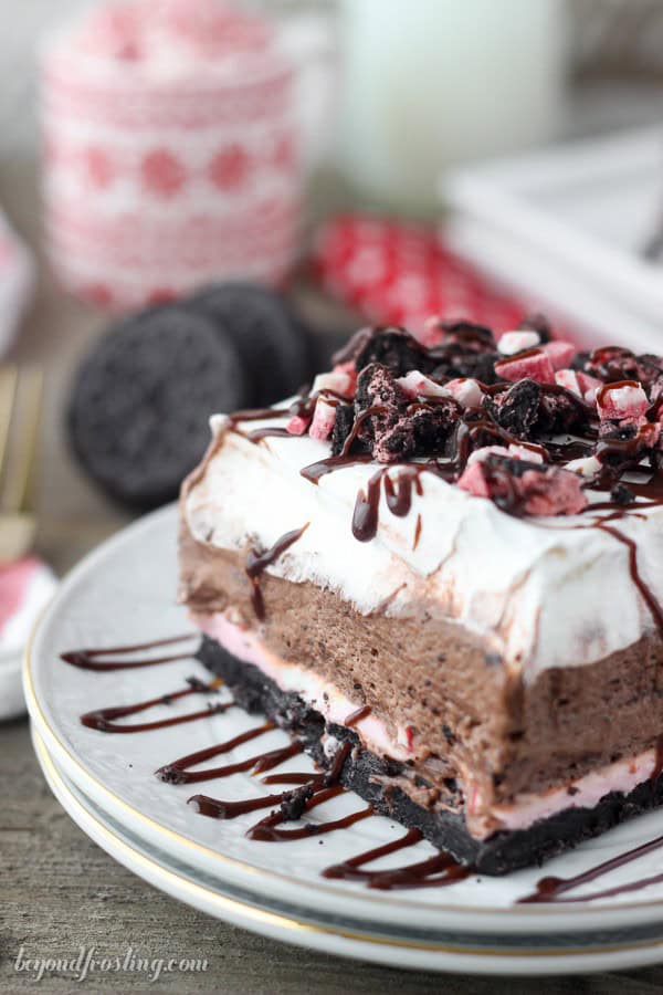 slice of dessert lasagna topped with hot fudge, Oreos, and peppermint candy on a plate