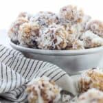 A vintage baking tray filled with coconut balls, and a few scattered on a wooden plank