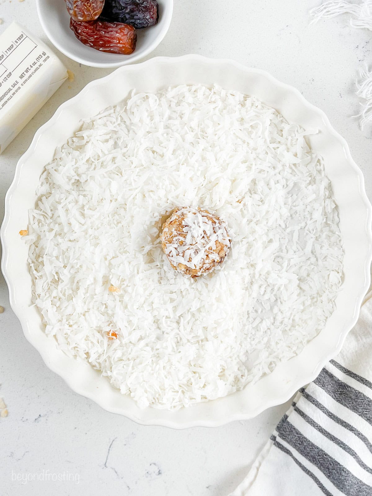 A date ball resting in a bowl of shredded coconut.