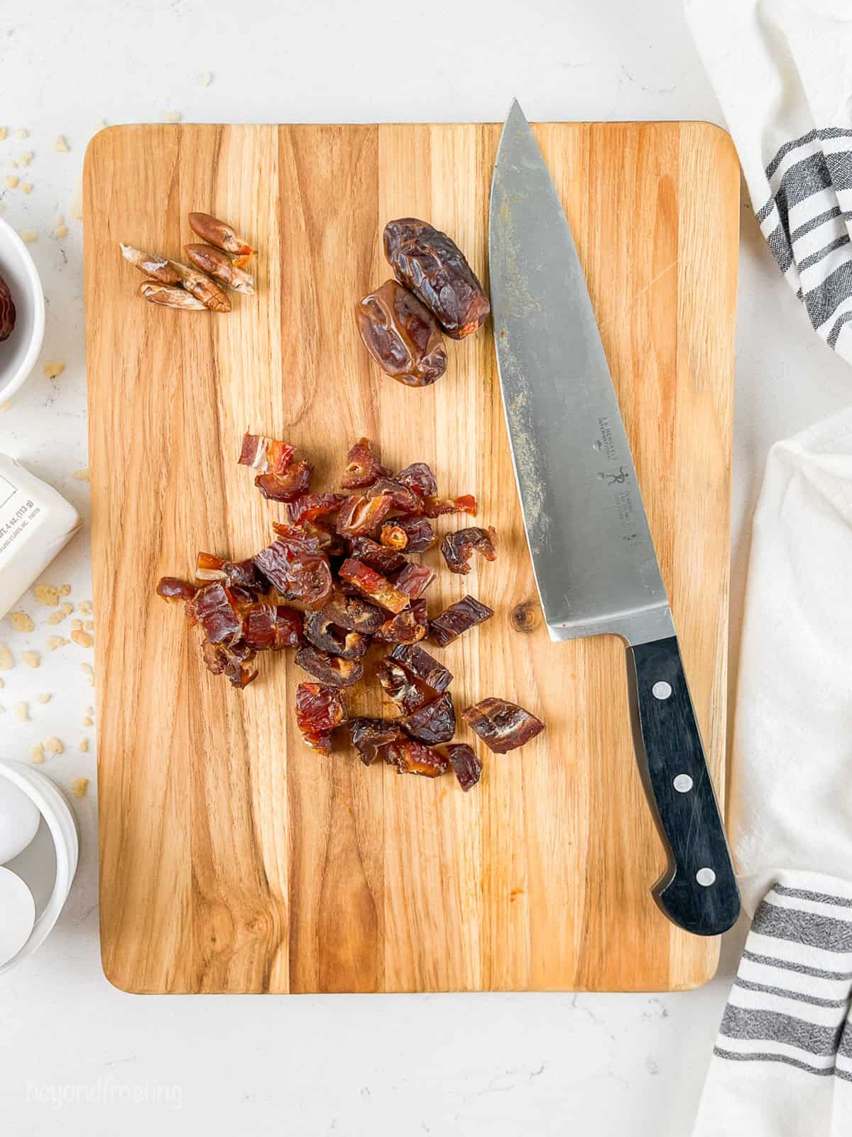 Overhead view of chopped pitted dates on a wooden cutting board next to a large knife.