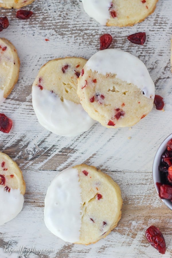 overhead of shortbread cookies half dipped in white chocolate on a distressed white board with dried cranberries scattered 