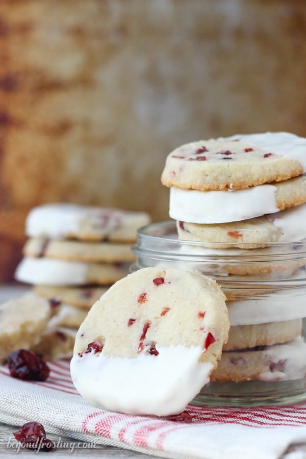 A stack of white chocolate dipped shortbread cookies in a glass jar, and another cooking leaning up against it