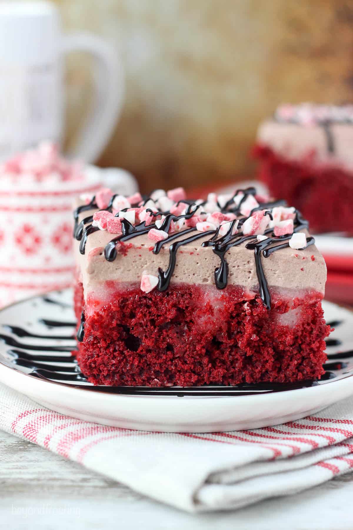 slice of red velvet poke cake garnished with peppermint crunch and hot fudge on a white plate